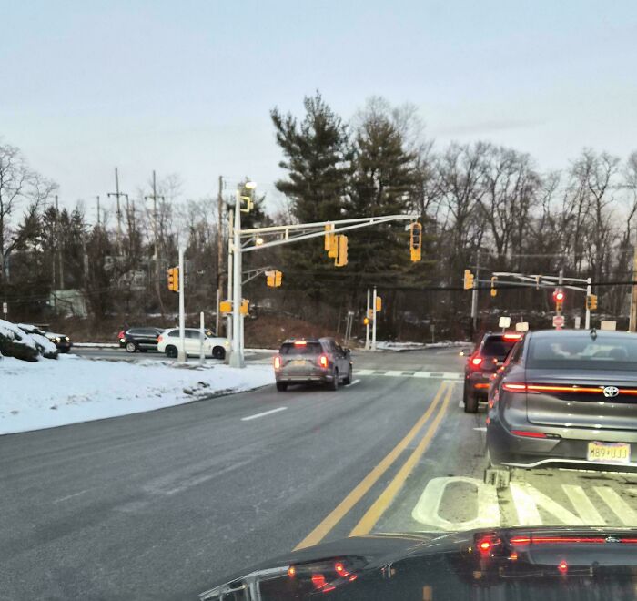 Cars stopped incorrectly blocking intersection at a snowy traffic light, showcasing dumb drivers in a busy suburban area.