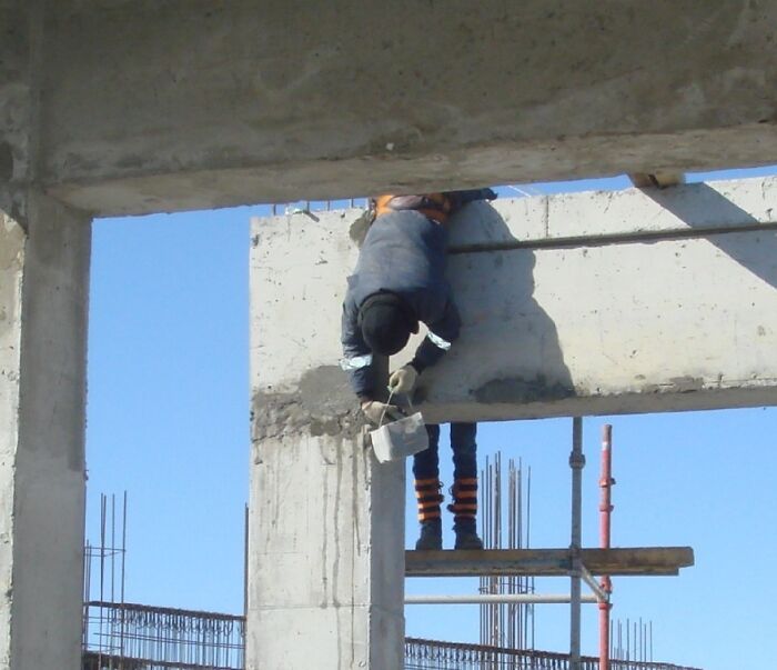 Construction worker in a reckless work moment hanging upside down on scaffolding without safety gear at a building site.