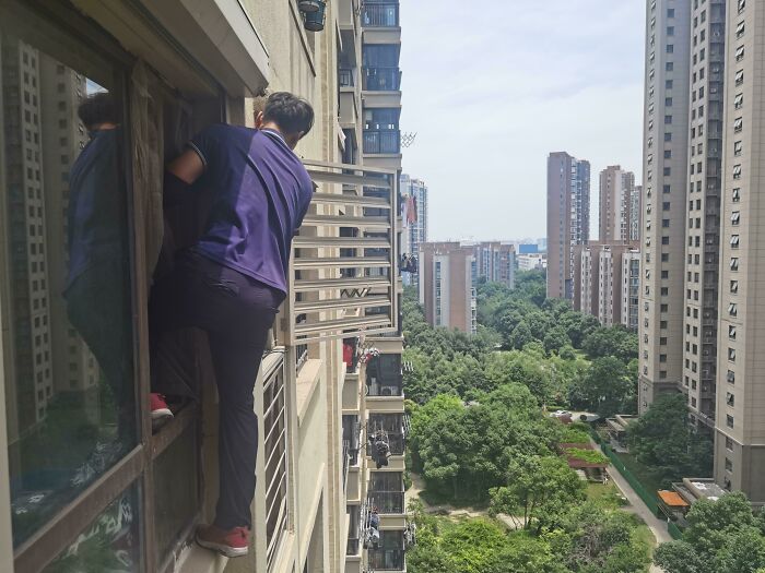 Man climbing outside high-rise building window in reckless work moment risking serious injury or death.