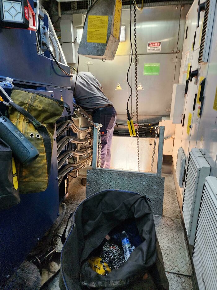 Worker bending dangerously near heavy machinery in a confined industrial space showing reckless work moments risk.