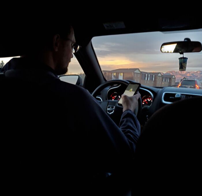 Man driving car while using smartphone at dusk, illustrating common examples of men being men behavior on the road.