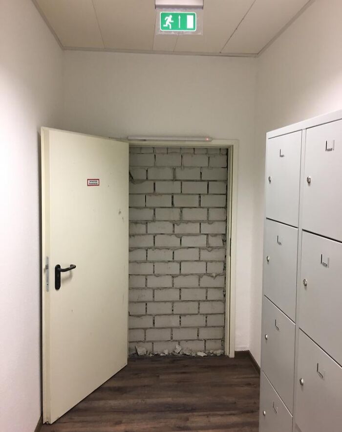 Hallway with an emergency exit door open to a blocked wall, illustrating reckless work moments affecting safety.