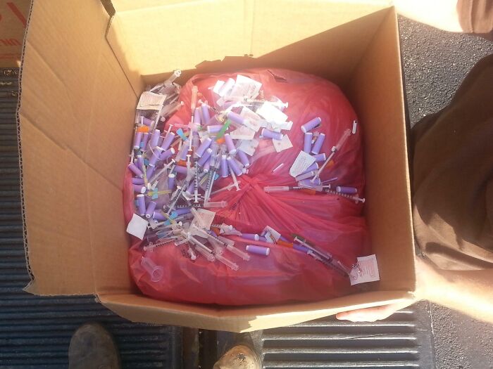 Box filled with used syringes and medical waste, illustrating reckless work moments needing safety awareness.
