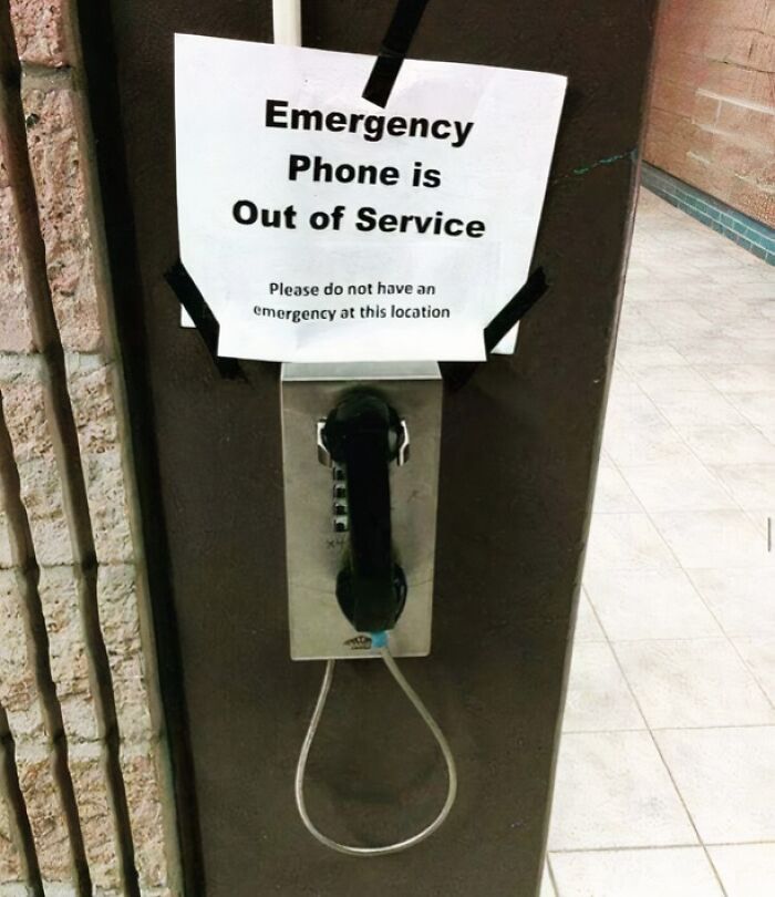 Emergency phone out of service sign taped above payphone, highlighting reckless work safety moment.