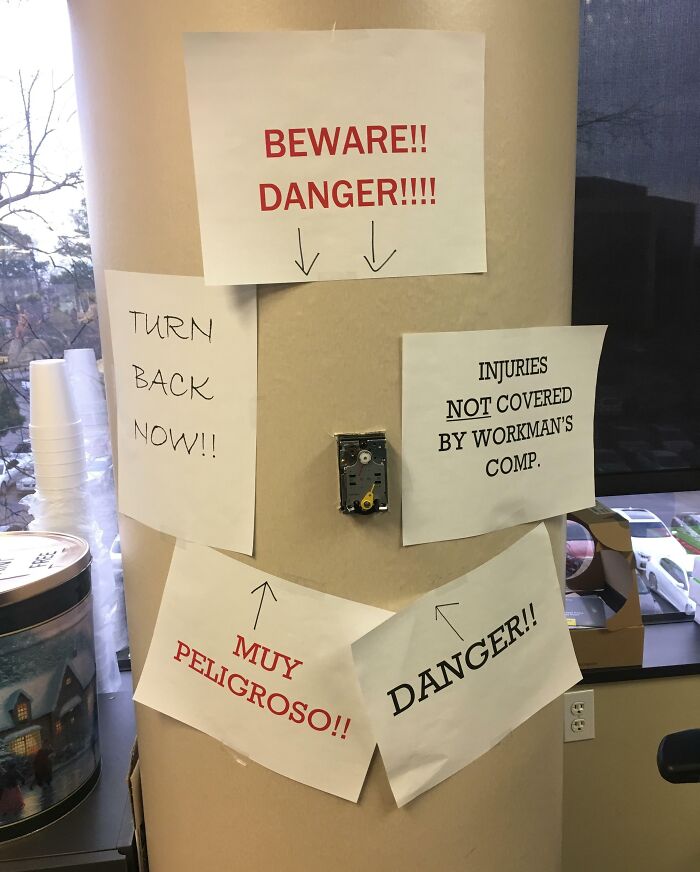 Multiple handwritten safety warning signs around an exposed electrical outlet highlight reckless work moments.
