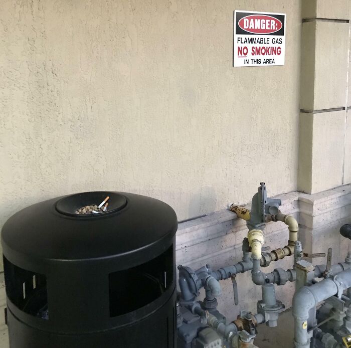 Trash can used as an ashtray near flammable gas pipes, illustrating reckless work moments and safety hazards.