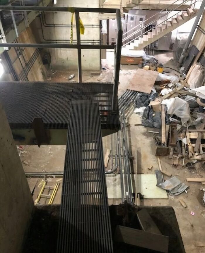 Reckless work moment showing an unsafe narrow metal walkway in a cluttered industrial construction site.