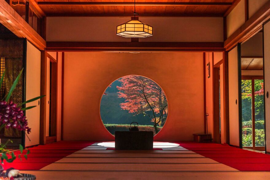 Traditional Japanese architecture interior with circular window showcasing autumn foliage outside in a serene setting.