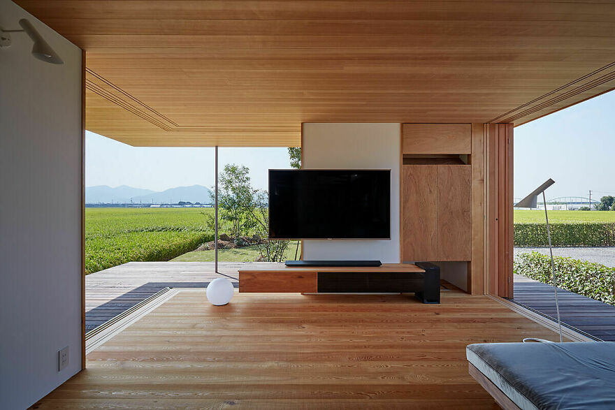 Minimalist Japanese architecture interior with wooden ceiling and floor, large glass windows showcasing serene outdoor landscape.