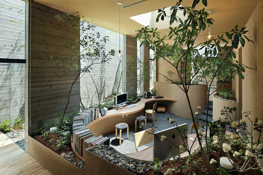 Modern Japanese architecture interior featuring natural light, curved wooden desks, indoor plants, and minimalist design elements.