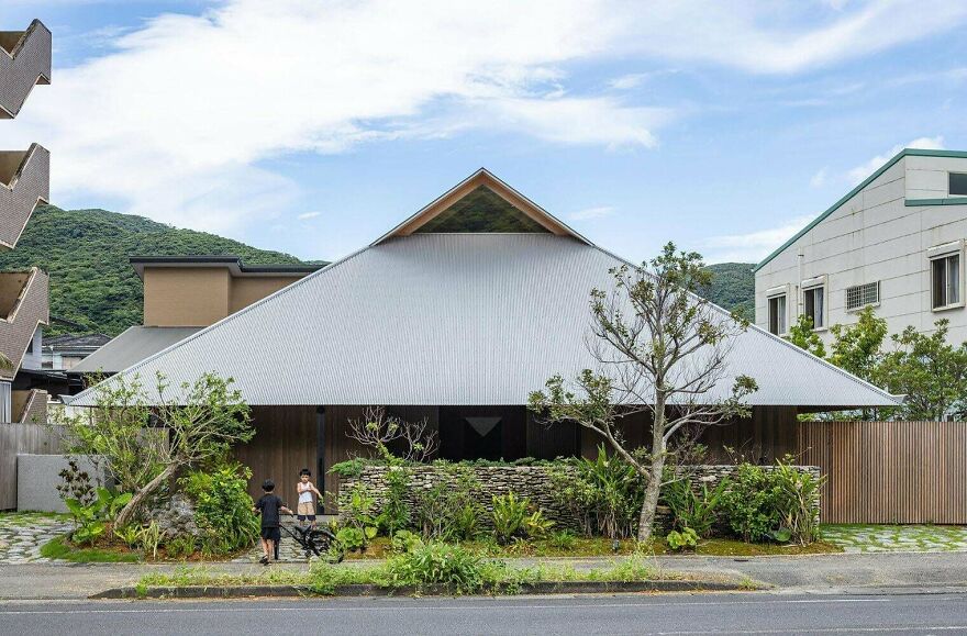 Modern Japanese architecture house with a large triangular roof surrounded by greenery and trees on a clear day.