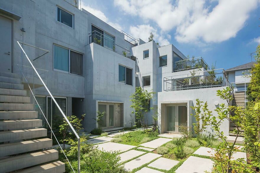 Modern Japanese architecture featuring clean concrete structures and a green courtyard under a bright blue sky.