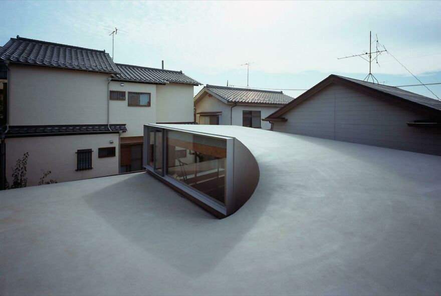 Modern Japanese architecture featuring a unique curved rooftop window amidst traditional residential buildings.