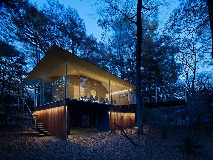 Modern elevated house with glass walls illuminated at dusk, showcasing unique elements of Japanese architecture in a forest setting.