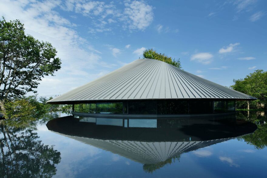 Modern Japanese architecture building with a sloped roof reflecting in surrounding water under a blue sky.