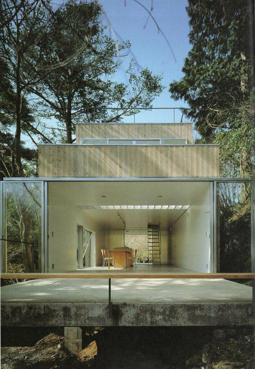 Modern minimalist house with open interior and wooden exterior surrounded by trees, an example of Japanese architecture.