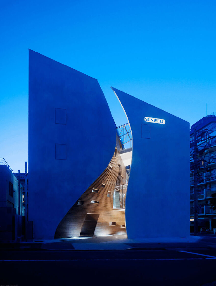 Modern Japanese architecture featuring curved concrete walls and illuminated wooden interior details at dusk.