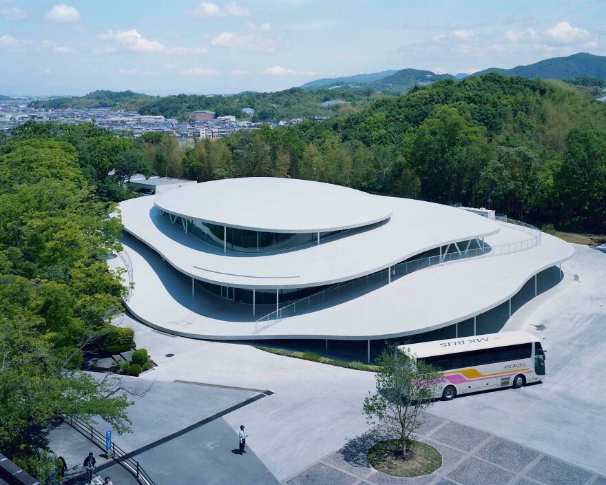 A modern, curvilinear building showcasing innovative Japanese architecture surrounded by trees and hills in the background.
