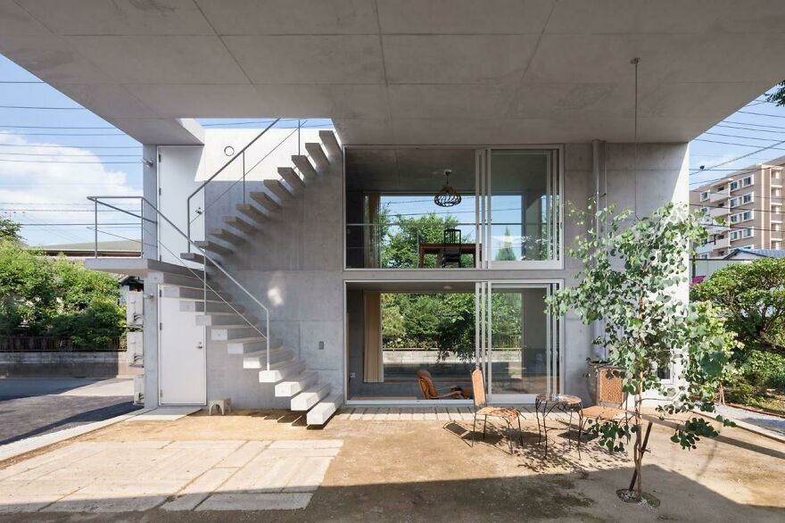 Modern Japanese architecture featuring concrete structure with open staircase and large glass windows showcasing indoor and outdoor spaces.