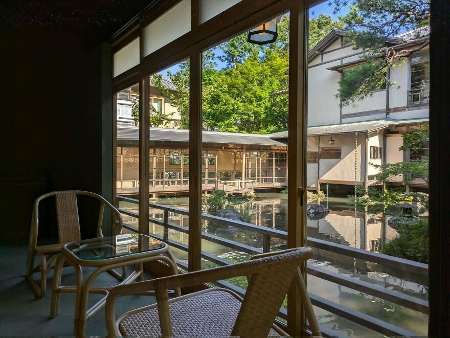 Traditional Japanese architecture featuring wooden structures surrounding a serene pond with outdoor seating area.