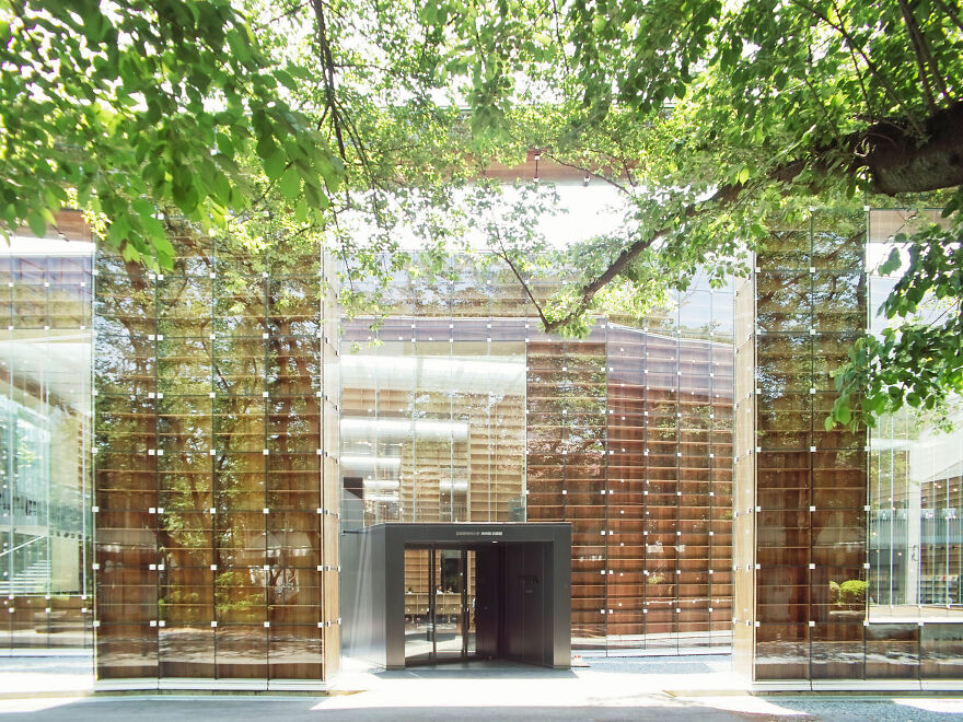 Modern building with glass facade surrounded by trees showcasing unique and interesting examples of Japanese architecture.