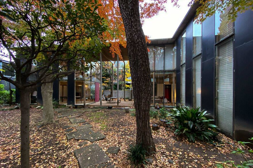 Modern Japanese architecture featuring a glass-walled house surrounded by autumn trees and a stone pathway in the garden.