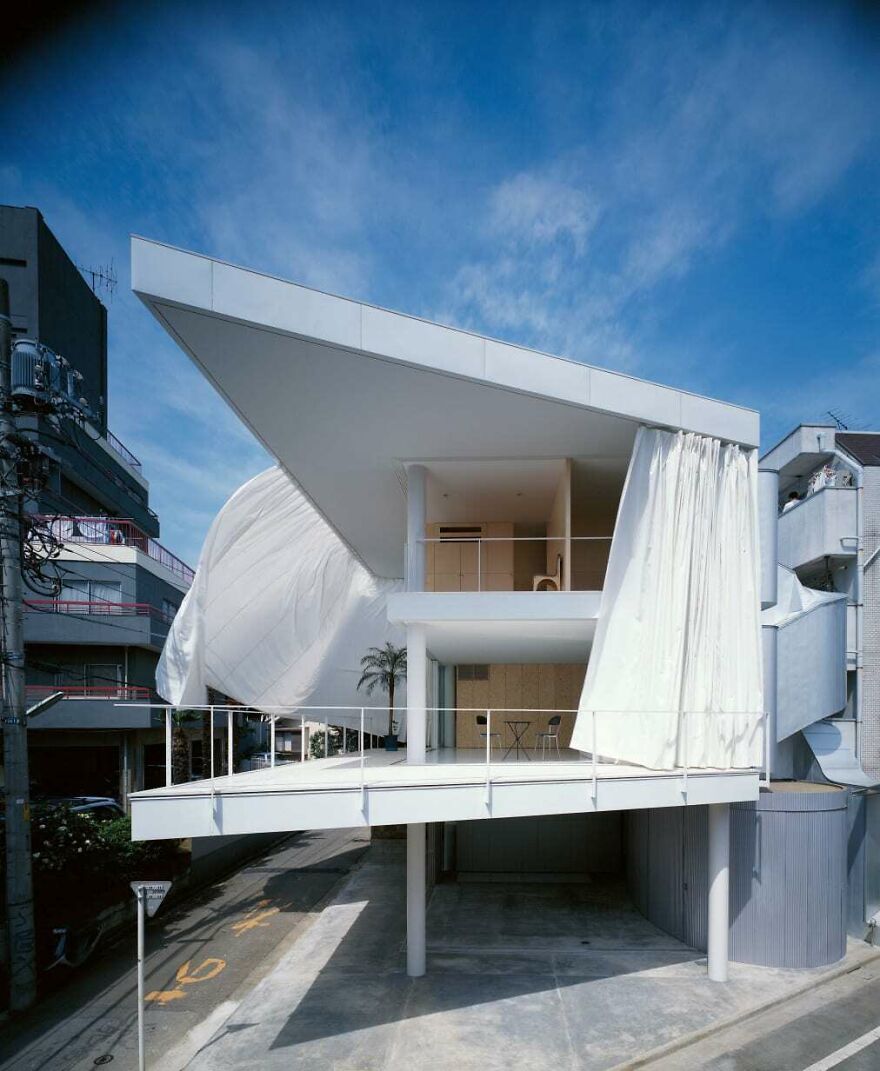 Modern white building with flowing curtains and sharp angles, showcasing unique Japanese architecture design in an urban setting.
