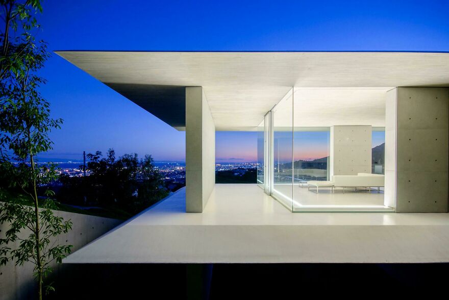 Modern Japanese architecture showcasing a minimalist house with glass walls and cityscape views at twilight.