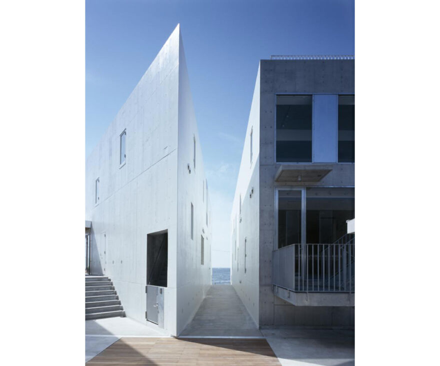 Minimalist modern Japanese architecture with sharp angles and concrete surfaces under a clear blue sky.