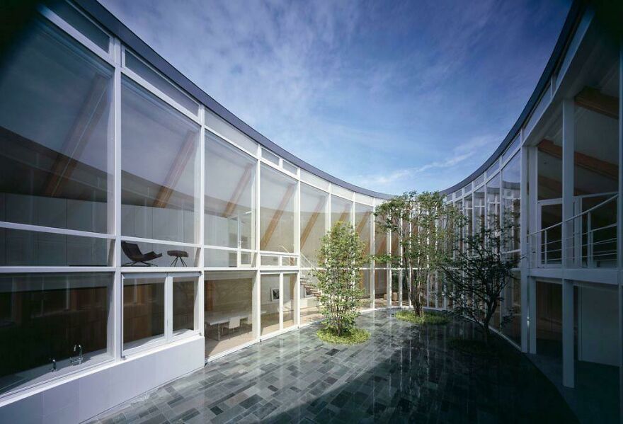 Modern Japanese architecture featuring curved glass walls and an open courtyard with trees under a clear blue sky.