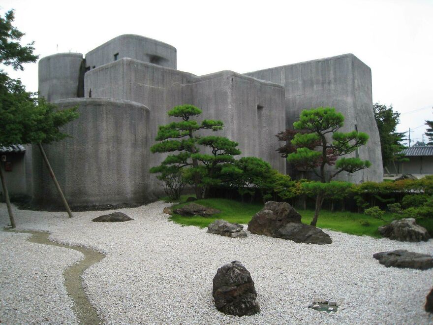 Modern Japanese architecture featuring minimalist concrete structures surrounded by traditional Zen garden elements and greenery.