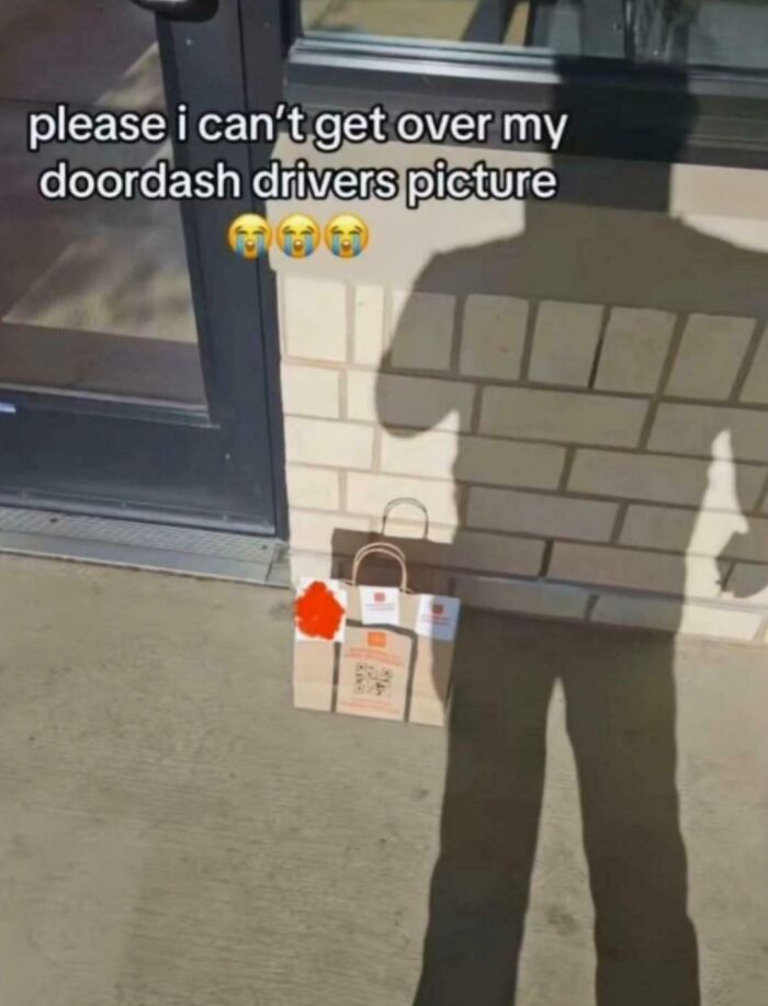 Shadow of a person resembling a dog stands by a DoorDash delivery bag outside a building in a funny screenshot.