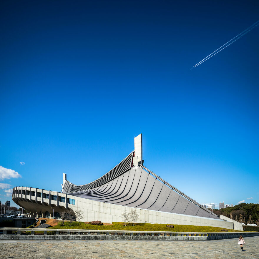 Modern curved structure showcasing unique Japanese architecture design under a clear blue sky with a jet trail above.