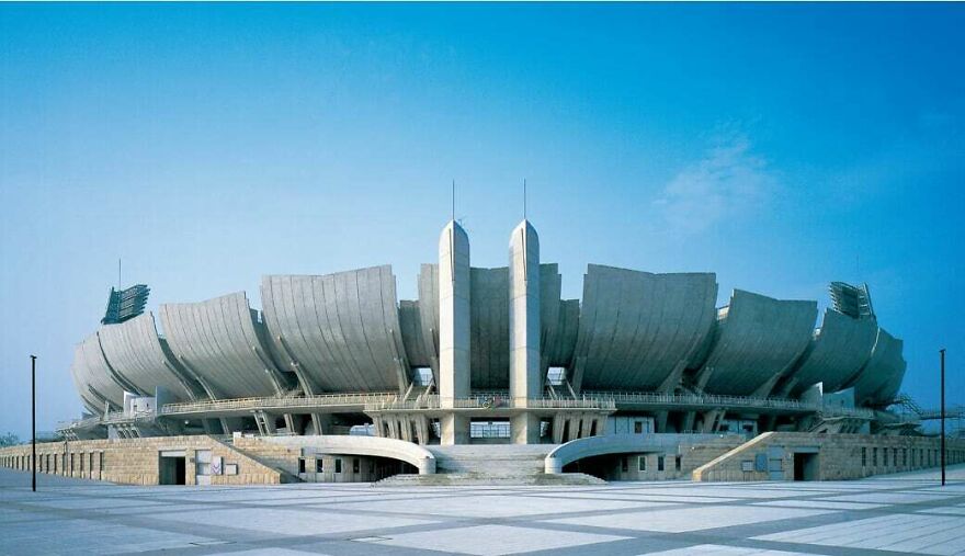 Futuristic stadium showcasing innovative Japanese architecture with curved concrete structures under a clear blue sky.
