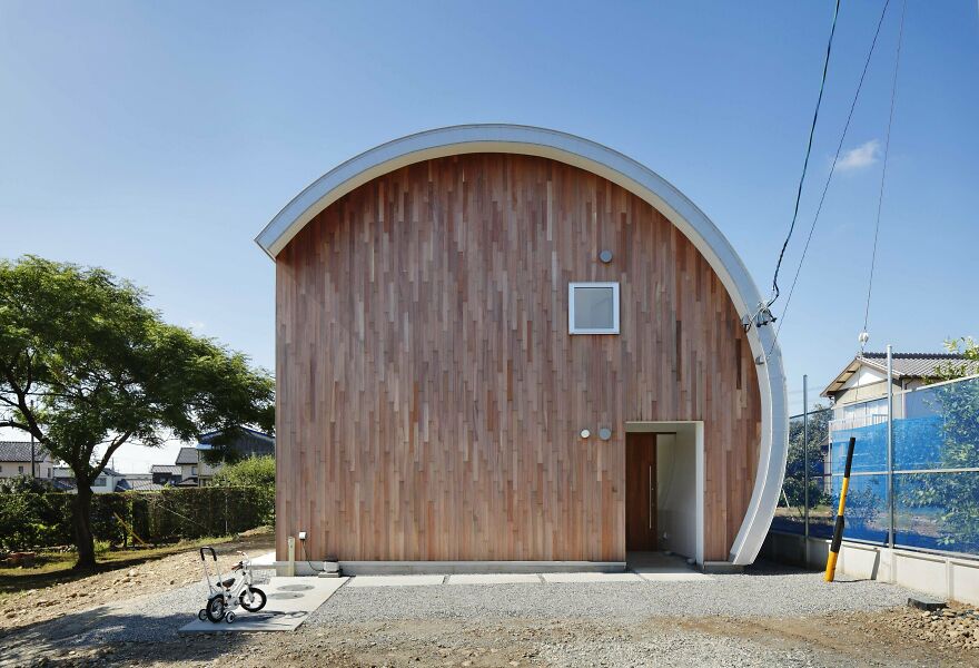 Modern house with curved roof and wooden facade showcasing unique Japanese architecture design under clear blue sky.