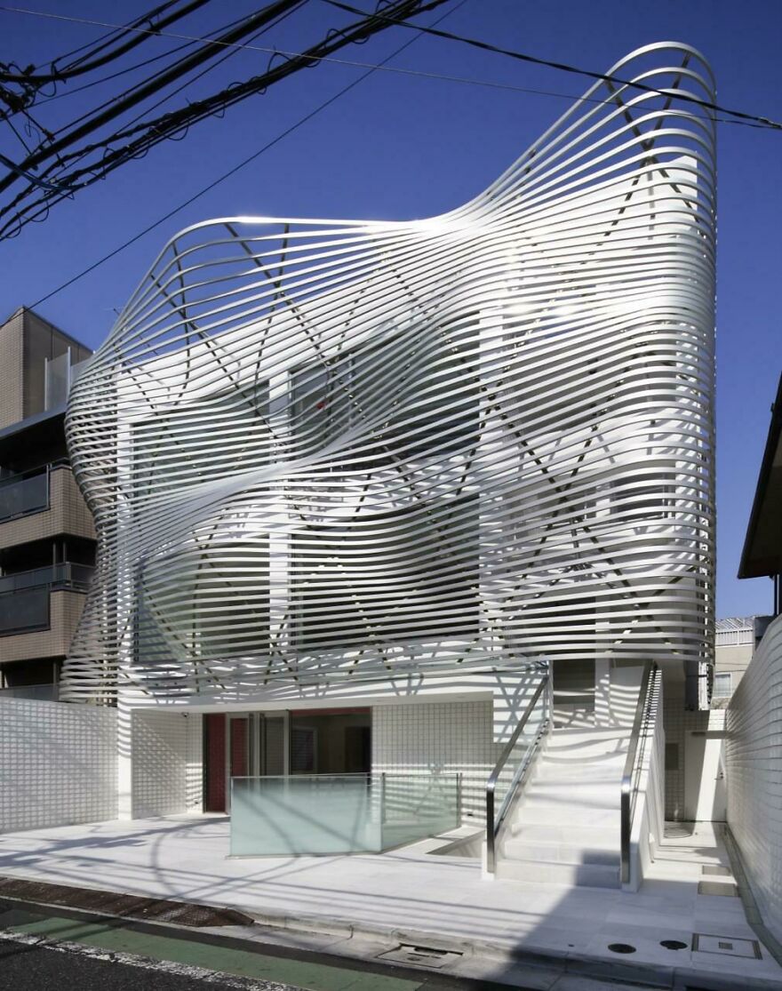 Modern building with curved metal slats creating wavy patterns, showcasing innovative Japanese architecture design.
