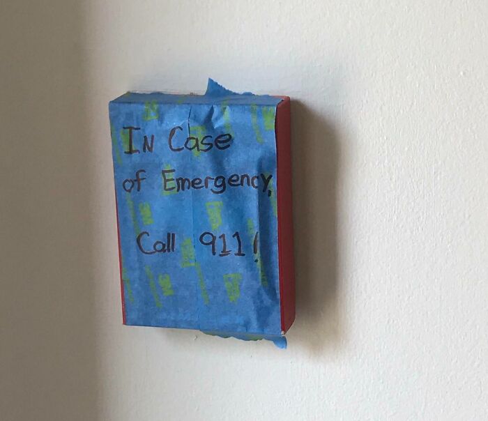 Improvised emergency call box covered with blue tape showing reckless work safety moment on a plain wall.