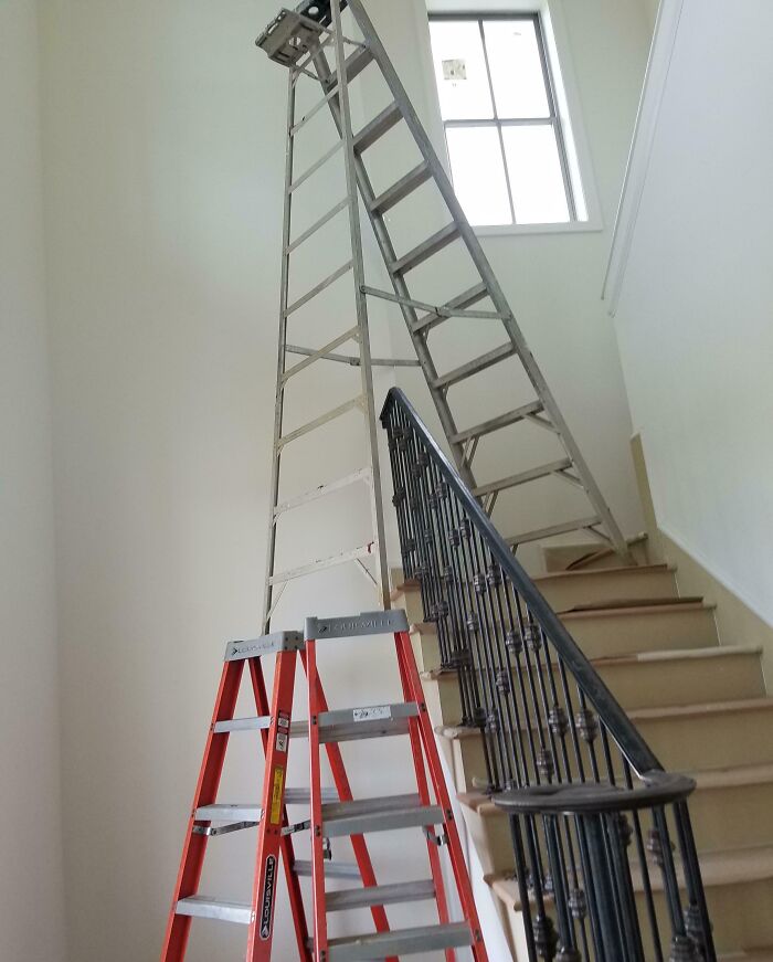 Tall metal ladder dangerously balanced on two other ladders on stairs, showcasing reckless work moments without proper safety measures.