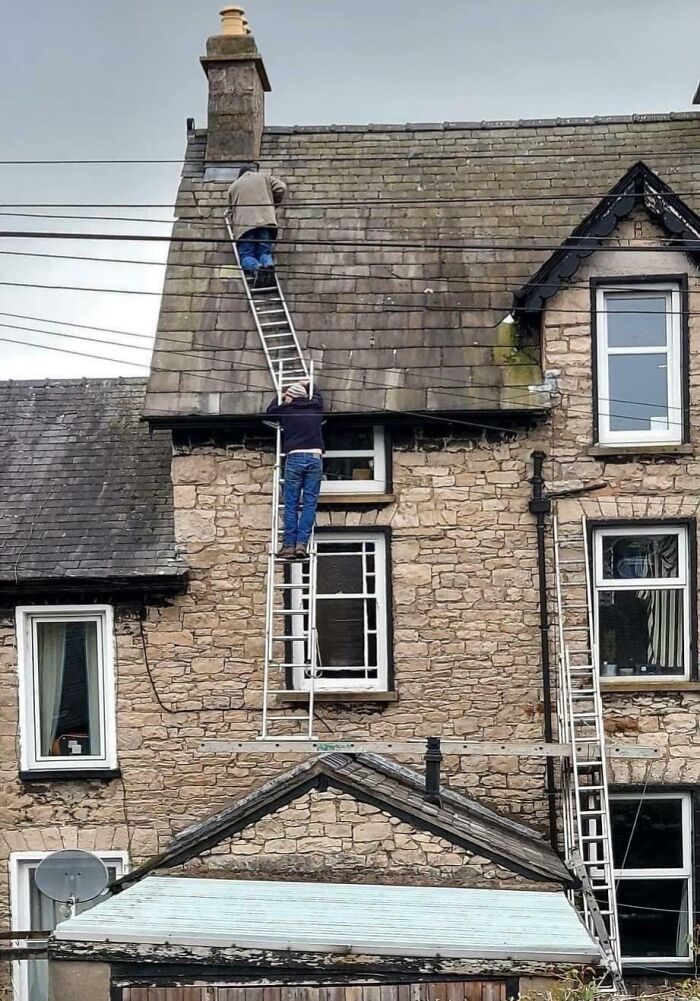 Two men on ladders precariously working on a roof, demonstrating reckless work moments without proper safety measures.