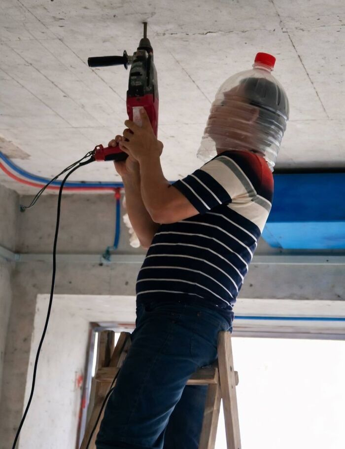 Worker with a plastic water jug on head using a power tool recklessly on a ladder in a construction site indoor setting.