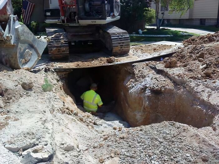 Construction worker in a hazardous trench under an excavator, illustrating reckless work moments risking safety on site.