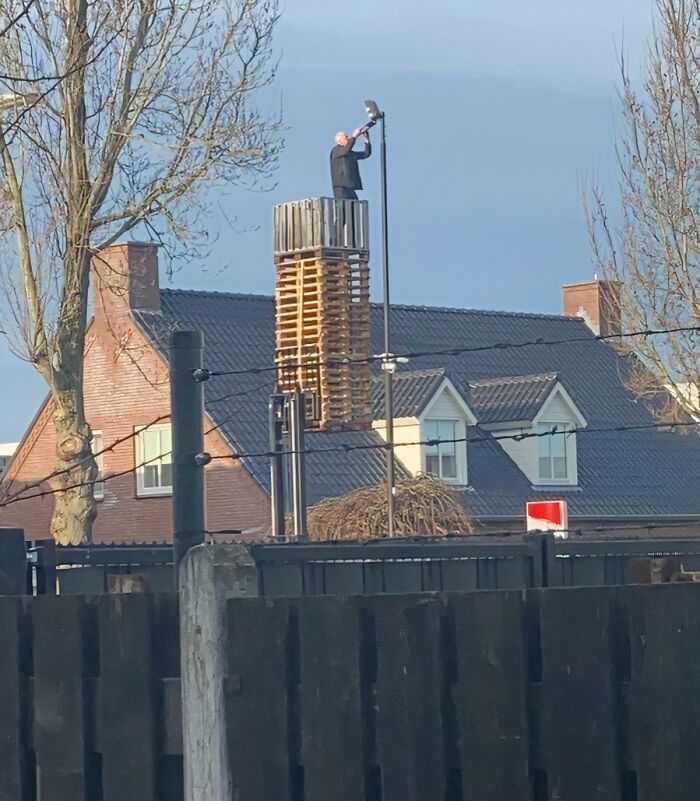 Man standing on stacked pallets fixing street light pole showing reckless work moments without safety gear outdoors