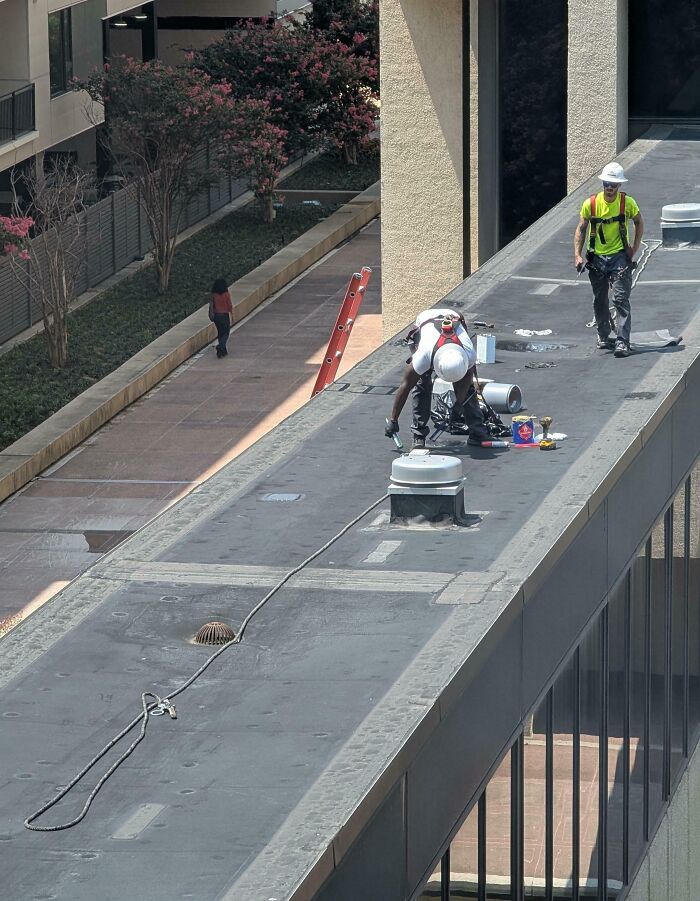 Two construction workers on a rooftop with safety gear missing, showcasing reckless work moments on building maintenance.