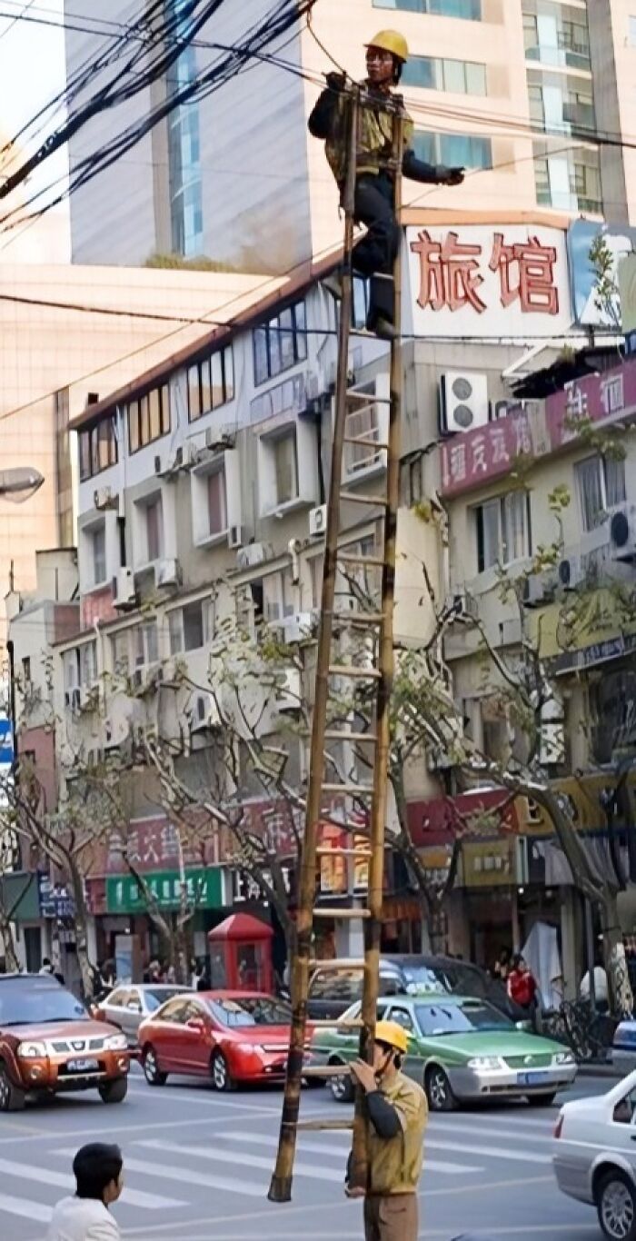 Worker climbing a tall, unstable ladder on a busy street, highlighting reckless work moments risking safety.