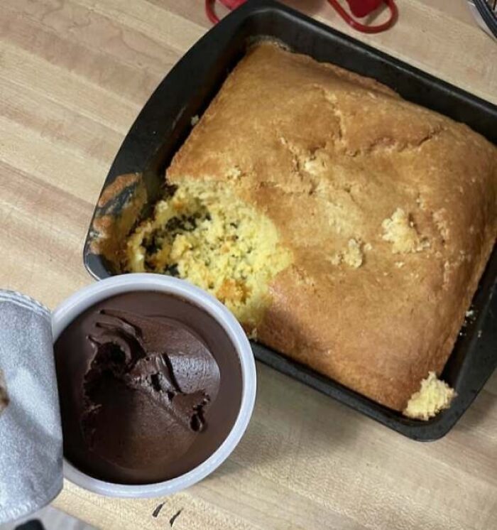 Partially eaten cornbread in a pan next to a container of chocolate frosting with a bite taken out, showing men being men.