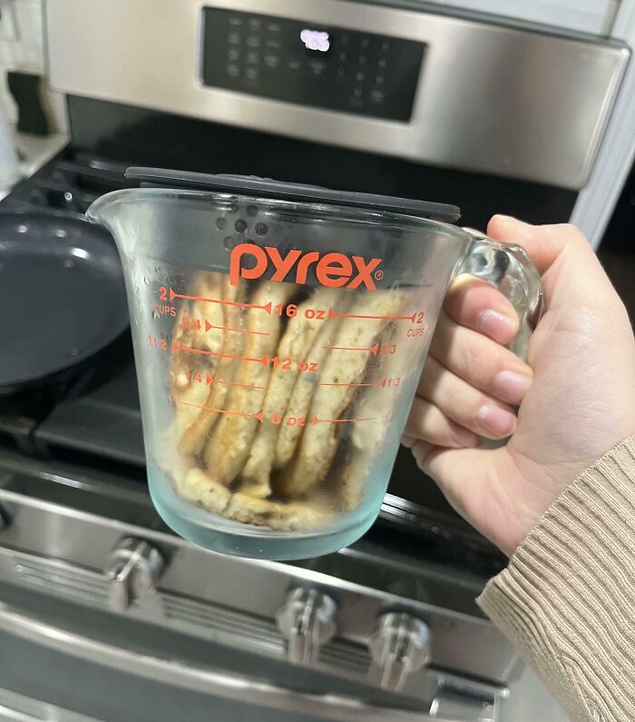 Hand holding a Pyrex measuring cup filled with stacked crackers, illustrating infuriating examples of men being men.