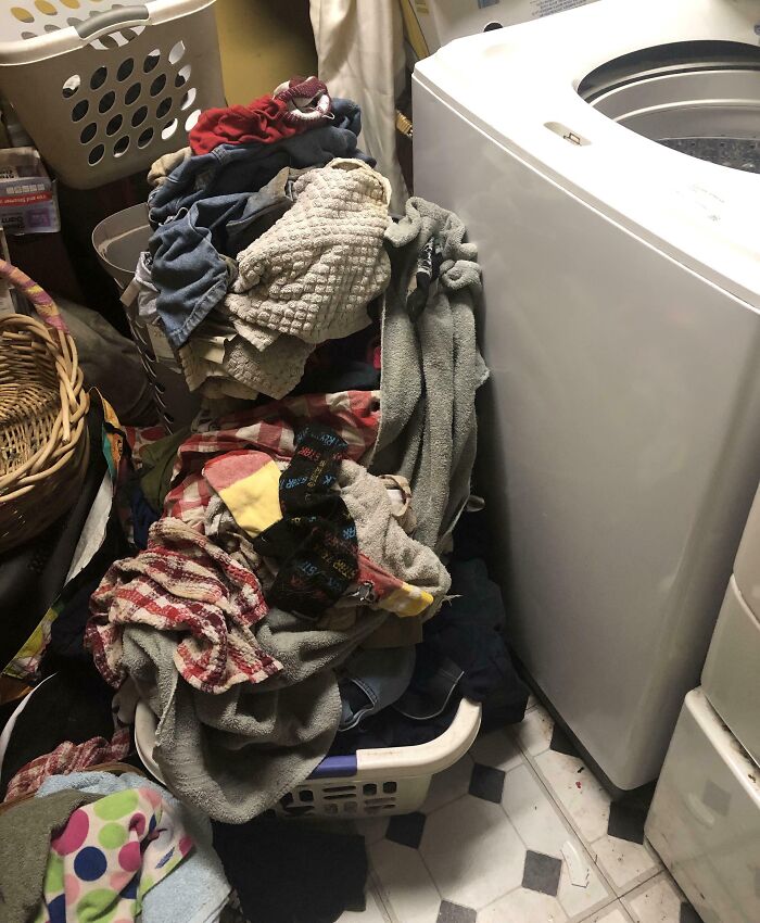 Laundry overflowing from baskets near washing machine, showing infuriating examples of men being men in household chores.