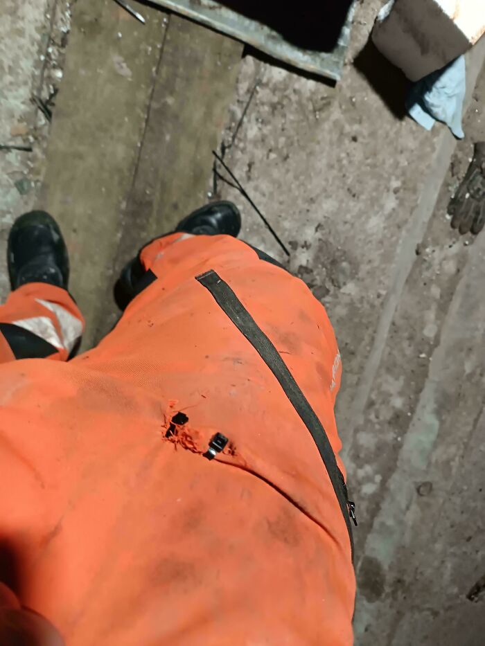 Close-up of torn orange work pants with a zip tie repair on a dirty floor, demonstrating if it's stupid but it works concept.