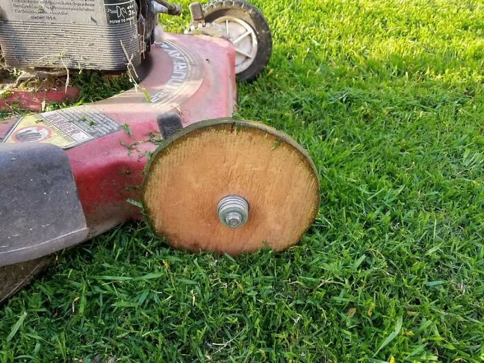 Lawnmower with a wooden wheel DIY repair demonstrating a clever if it's stupid but it works solution on green grass.