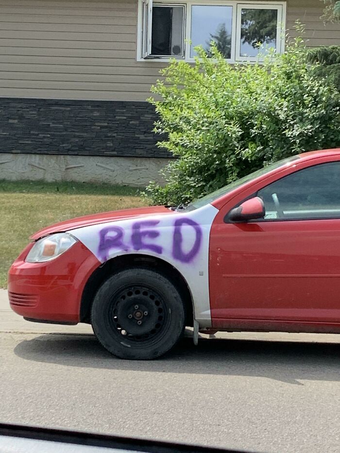 Red car with a mismatched white front panel spray painted with red in purple, an example of if it's stupid but it works.